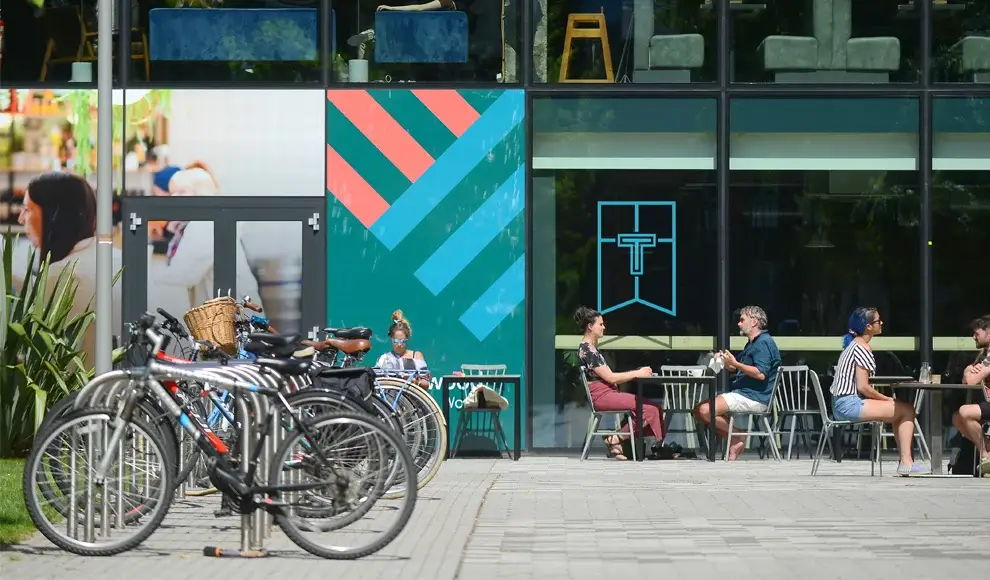Some bikes in a bike rack and people sat outside a bar on AMBS campus