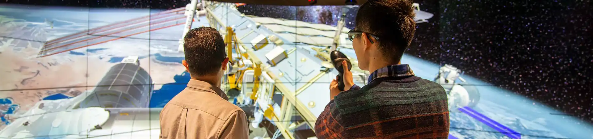 Two students in front of a large screen showing a spacecraft over earth