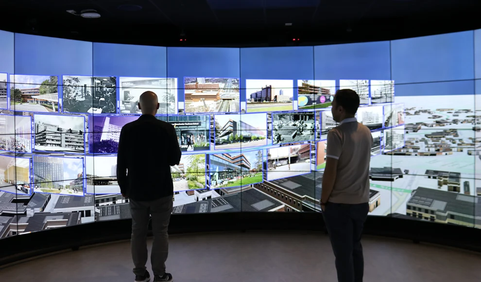 Two men stood in front of a large panoramic screen displaying data in the Data Visualisation Observatory at AMBS