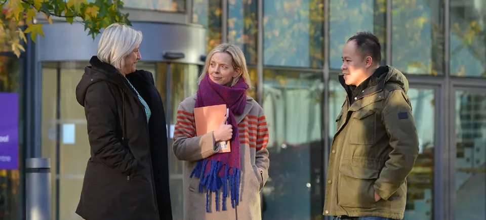 Three AMBS colleagues stood outside the school building having a conversation