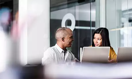 Two colleagues smiling at each other sitting down at a desk in an office