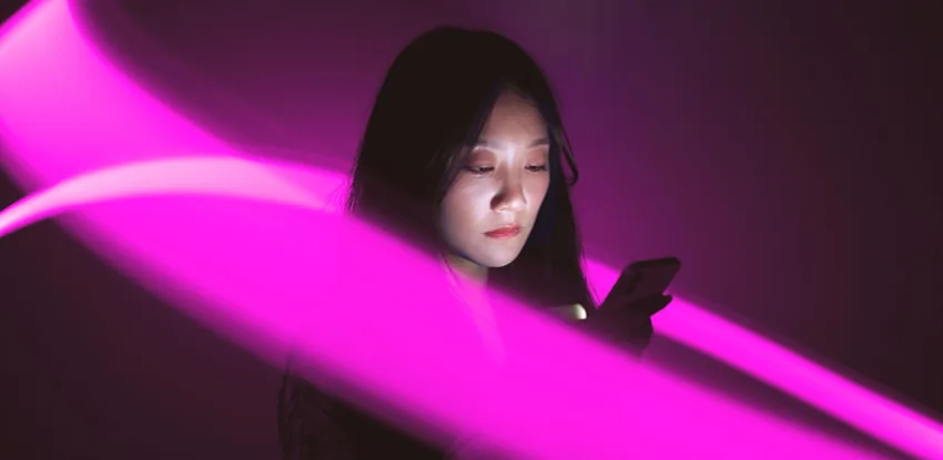 A woman looking at her smartphone whilst being surrounded by a stream of purple light.