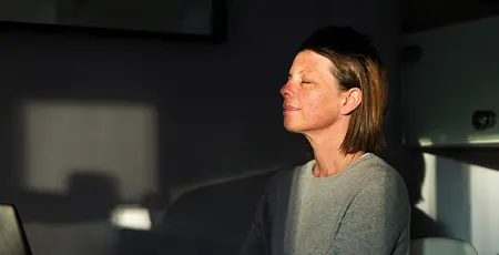 Woman closing her eyes as the last sun rays of the day come into her house