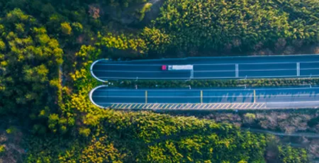 An aerial view of a lorry driving down a road surrounded by trees