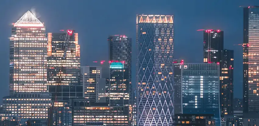 An aerial view of multiple tall buildings in the Canary Wharf skyline at night