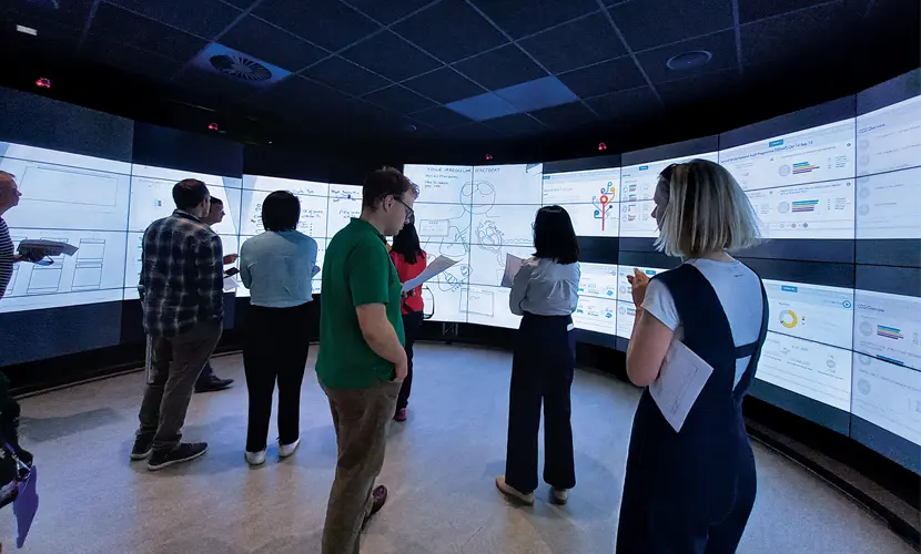 A group of professionals stood in front of interactive screens in the Data Visualisation Observatory at AMBS.