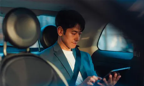 Asian male entrepreneur working on digital tablet while traveling by a car.