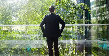 A man standing on a balcony looking out over lots of greenery.