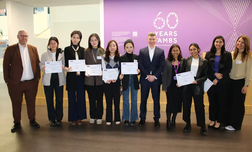 A group of HR master's students standing with some HR professionals and holding certificates.