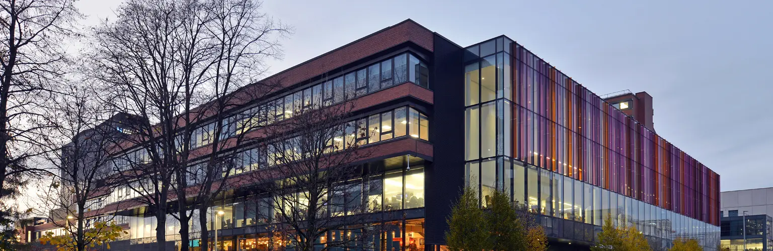 Alliance Manchester Business School building with a tree in front of it in the evening light.