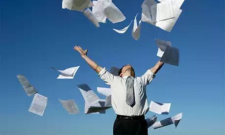 A businessman throwing papers up in the air outside on a sunny day