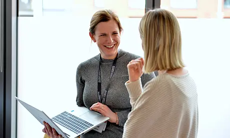 Two professional business women chatting whilst holding a laptop